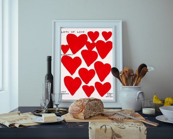 Un tableau avec des coeurs rouges est affiché dans une cuisine rétro et minimaliste. Sur le plan de travail il y a du pain, des ustensiles de cuisine et du beurre. 