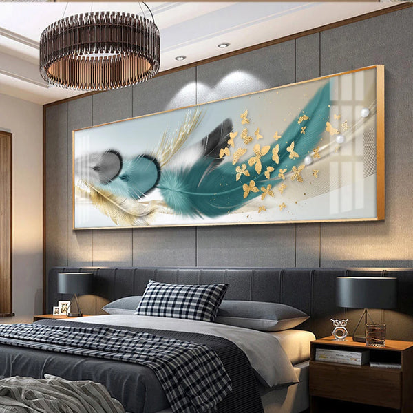 Dans une chambre au style moderne chic, une toile en format paysage avec des plumes dorées, bleues et grises ainsi que des papillons dorées est installée au dessus du lit. 