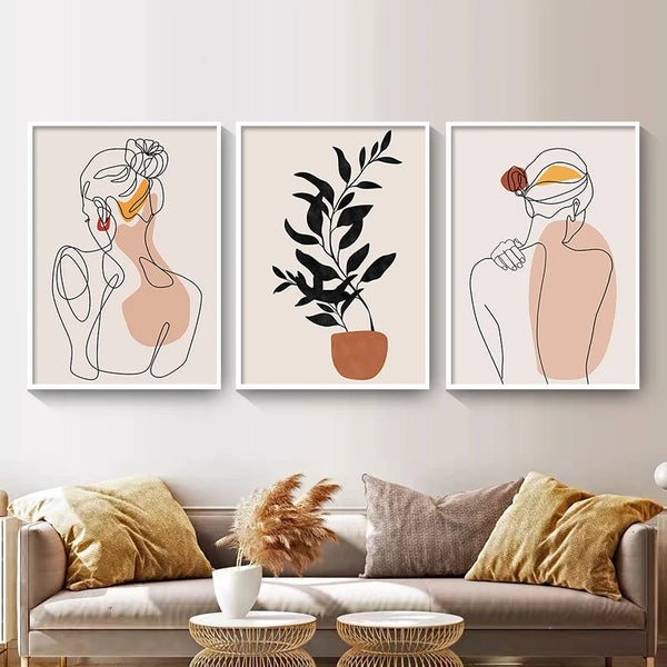 Dans un salon au style scandinave et bohème, trois toiles sont installées. Il y a deux femmes dessinées en traits noirs avec des tâches colorées et au milieu une plante colorée. 