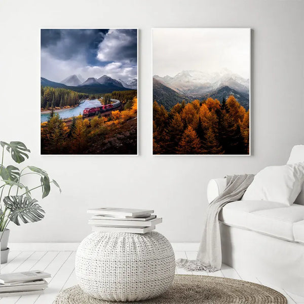 Dans un salon au style blanc bohème, deux toiles de paysage de forêt en automne sont affichées au mur. En dessous il y a un pouf, un canapé blanc et une plante.