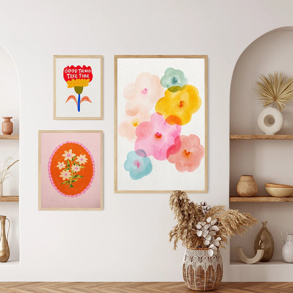 Dans un salon avec un style bohème blanc et bois, trois toiles sont affichées. Les toiles représentent des peintures folkloriques bohème de fleurs. 