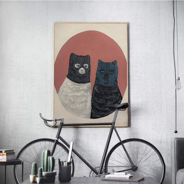 Dans un salon de style industriel, une toile représentant deux chats cagoulés est affichée. 