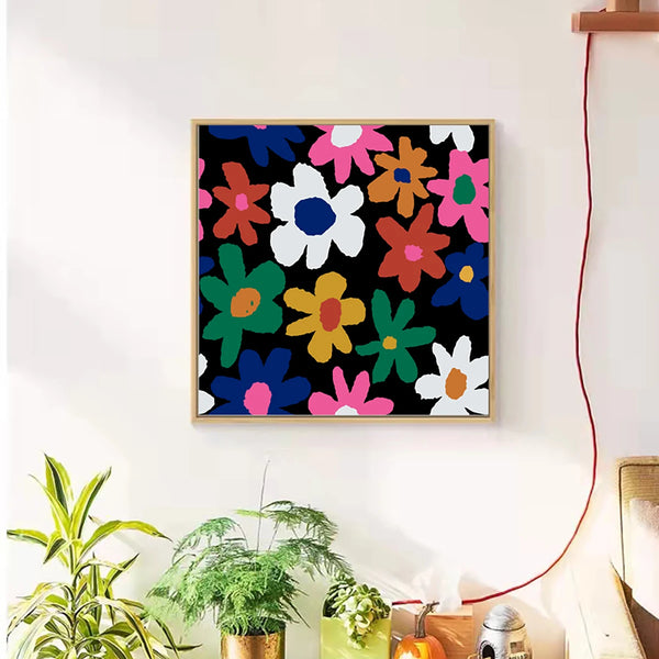 Dans un salon de style scandinave et rétro est affichée une toile avec fond noir et fleurs simples colorées. Il y a des plantes en dessous. 