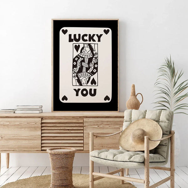 Dans un salon bohème, une toile représente la carte dame de coeur notée Lucky you en noir et blanc est affichée.