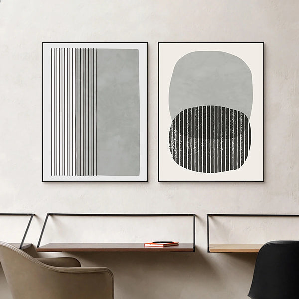 Dans un espace de travail avec plusieurs bureau, deux toiles dans les tons de gris et noir sur fond blanc sont affichées. L'une des toiles est composé de lignes et de rectangles tandis que l'autre est composé de cercles uniformes et de lignes. 