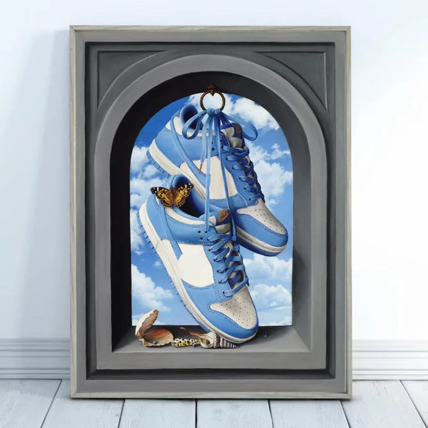 Dans une pièce épurée, est posé au sol un tableau de style classique avec des sneakers blanches et bleues avec des papillons et des coquillages est affiché. 