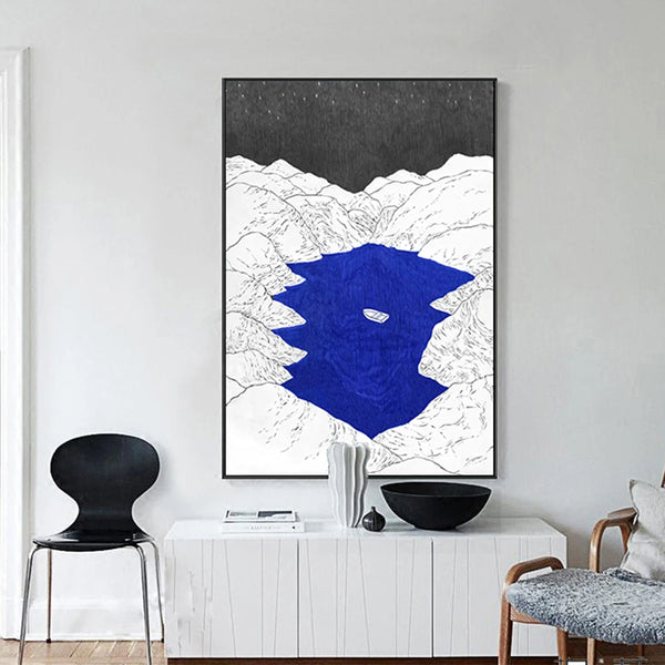 Un tableau d'un dessin noir et blanc de montagne avec un lac bleu klein au milieu est affichée dans un salon de style moderne et épuré. 