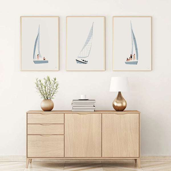Dans une pièce au style épuré et scandinave, trois toiles sont affichées. Elles représentent chacune un voilier dans un style minimaliste épuré. 