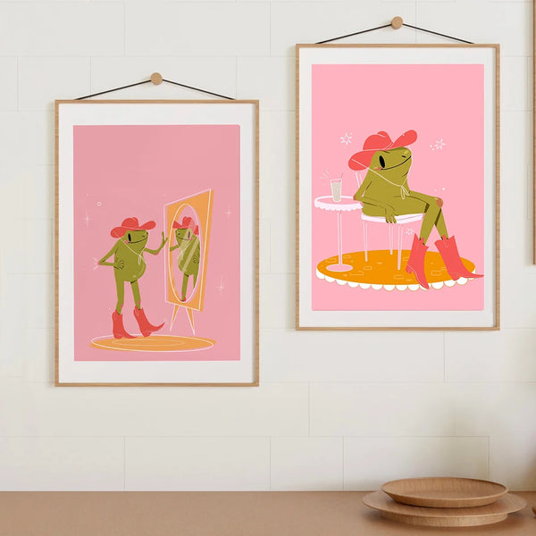 Dans une cuisine épuré et scandinave, deux toiles roses avec une grenouille verte tendance et girly déguisé en cowboy sont affichées. 