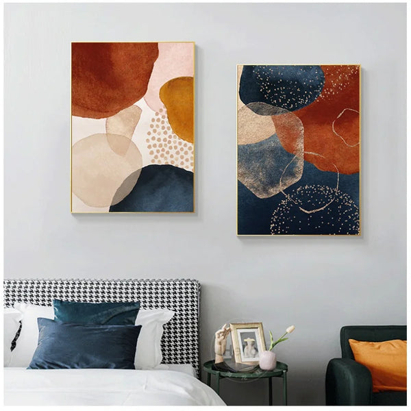 Deux tableaux scandinaves avec des tâches abstraites colorées sont affichées dans une chambre. Il y a un lit avec une décoration très design. Les couleurs des tableaux sont bleus, roses et rouilles.