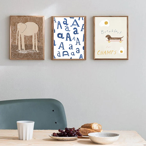 Dans une cuisine scandinave et épurée, trois toiles sont accrochées au mur. Les toiles sont dans un style minimaliste et enfantin représentant un éléphant, un chien et la lettre A. 