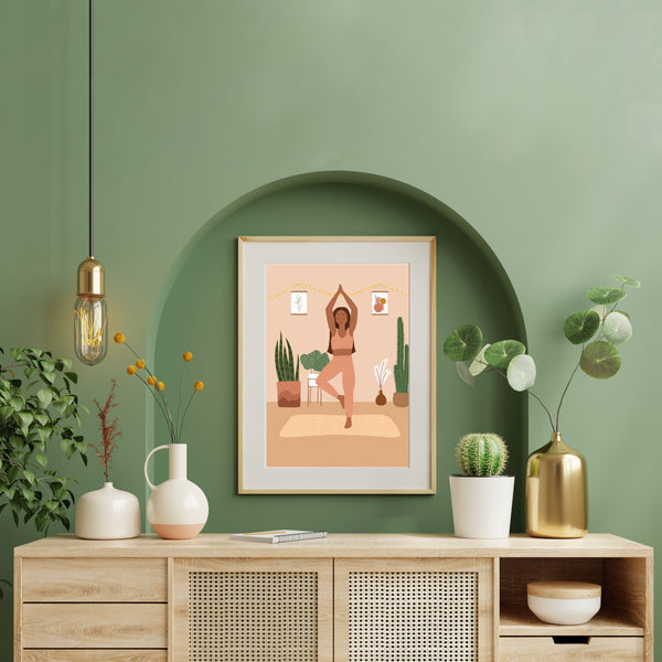 Dans une pièce au mur vert et à la déco nordique est accroché une toile représentant une femme faisant du yoga avec des plantes autour. 