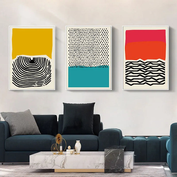 Il y a trois tableaux avec des formes géométriques bicolores dans un salon au dessus d'un canapé. Le style est scandinave. 