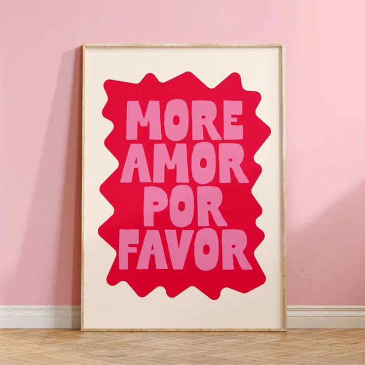 Un tableau blanc est posé droit contre un mur rose sur un sol en parquet. Il y a une forme rose fucshia sur laquelle est écrit en rose plus clair "More amor por favor"