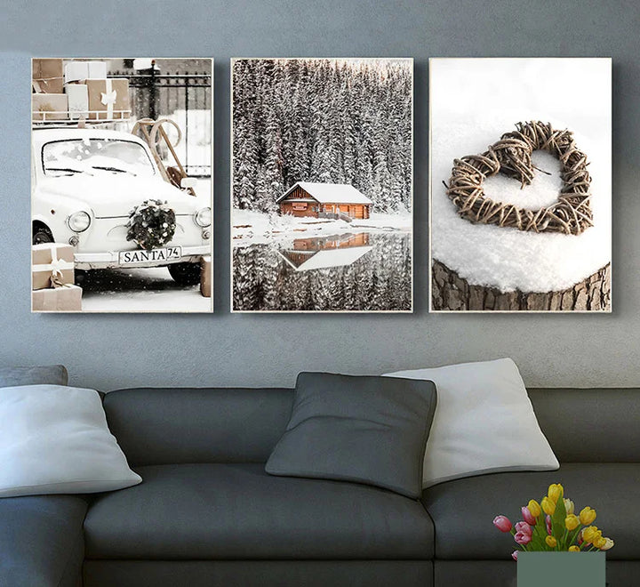 Trois toiles sur le thème de noël avec un chalet, un coeur et une voiture entourés de neige, sont affichés dans un salon où il y a un canapé gris. 